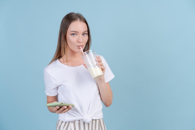 Girl stands with cocktails and smartphone on copy blue background in studio