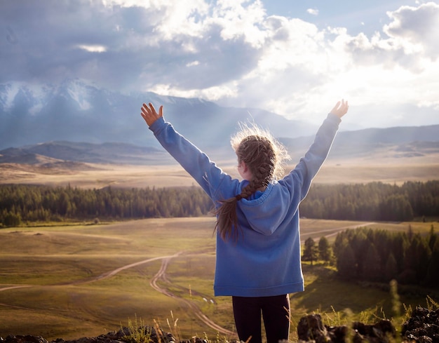 girl stands with her back against the backdrop of a mountain landscape