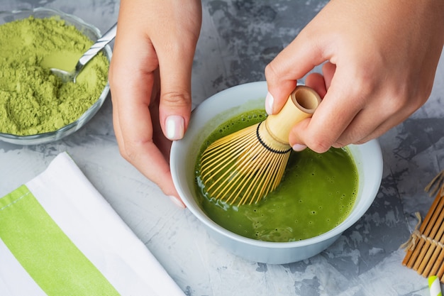 Girl stirs matcha green tea a bamboo whisk. The process of making tea close-up