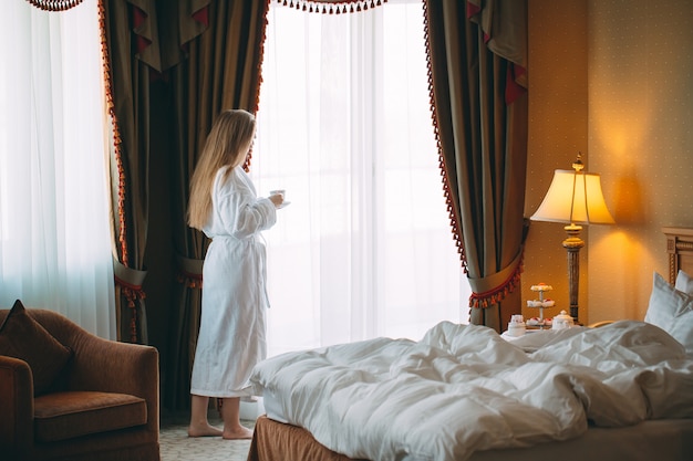 The girl Stit near the window and drinks morning coffee in the hotel room or at home.