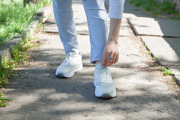 The girl straightens the laces of her shoes on the street