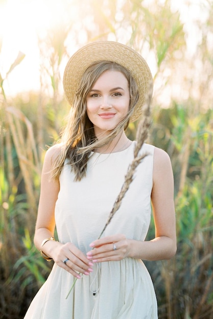 Girl in a straw hat stands with a dry cane in her hand