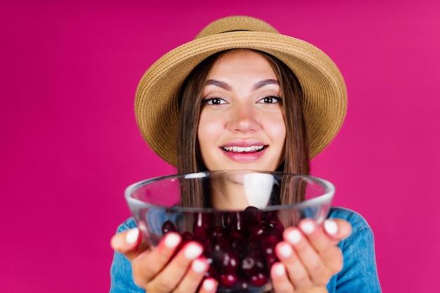 Girl in a straw hat with a friendly smile holds out a vase with cherry berries