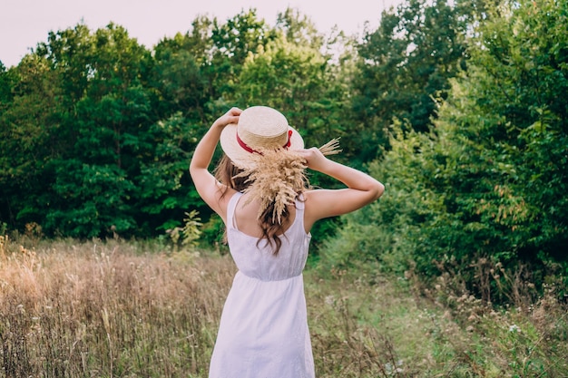 Girl in a straw hat with her back to the photographer. Girl in a white dress on a summer sunny day.