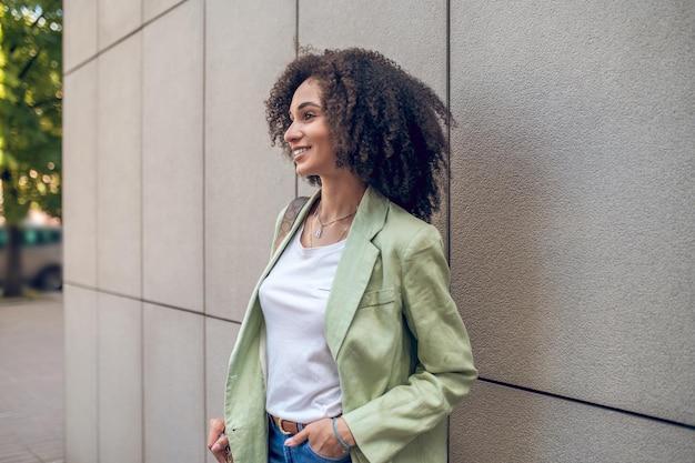 Girl in the street. Pretty curly-haired woman standing near the wall in the street