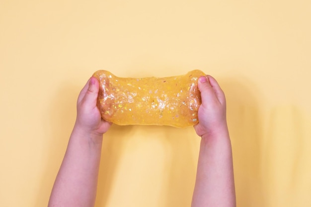 Girl stretching colorful orange slime on the sides Children's hands playing slime toy on an orange background