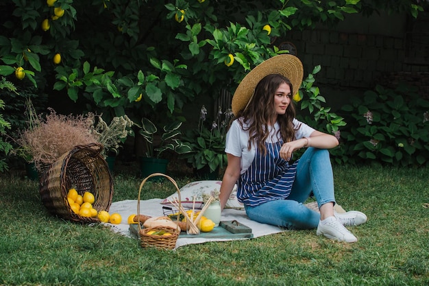 A girl in a striped apron and a straw hat sits on the grass near the house