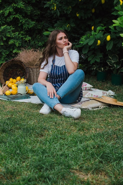 A girl in a striped apron and a straw hat sits on the grass near the house