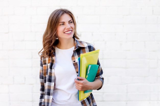 Girl student holds folders and a notebook in her hands and smiles