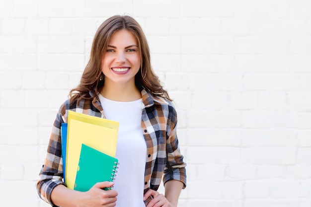 Girl student holds folders and a notebook in her hands and smiles