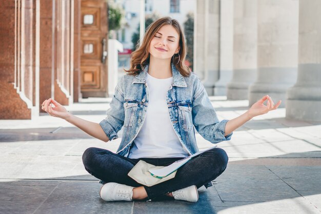 Girl student sitting on the floor and meditating. Lovely girl asks for a good grade in the exam. Girl prays in lotus position.