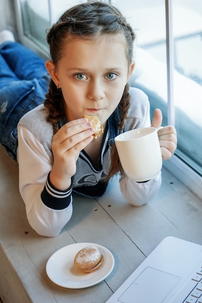 Girl student study online with video call teacher, Happy young girl listen lecture watch at laptop at home and drink tea and eat cookies. Covid-19 coronavirus.