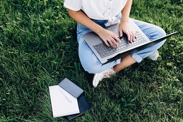 Girl student with a laptop outdoors sits on the grass in the park