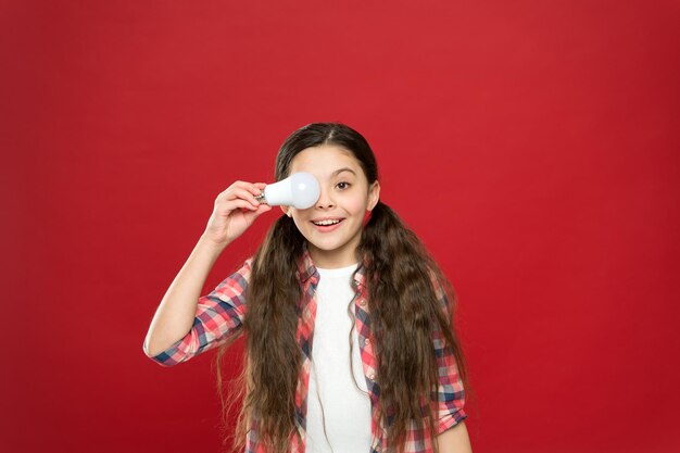 Girl of success. cheerful child girl. little child hold light idea bulb. education concept. small school kid red background. small girl lightbulb. energy and electricity. creating a great idea.