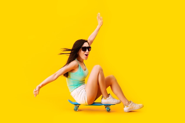 Girl in sunglasses, sitting on a skateboard, over yellow space