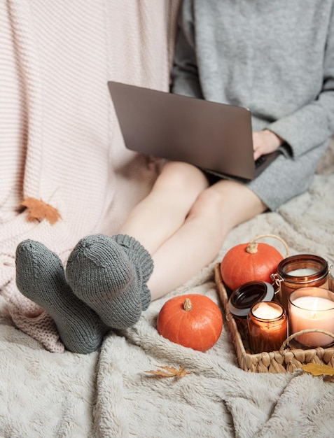 A girl in a sweater and knitted socks sits on a blanket and works on a laptop