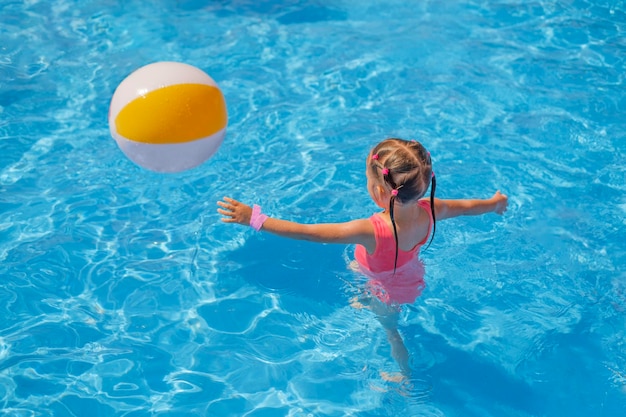 Girl in swimsuit runs after an inflatable ball in pool