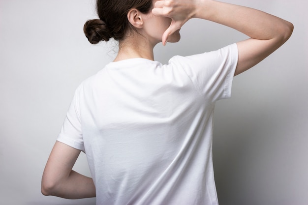 A girl in a T-shirt stands and points a hand to the back. Blank for branding.