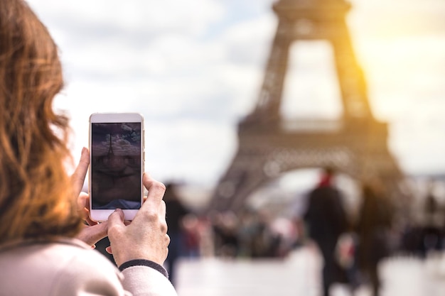 Girl takes pictures of a Eiffel Tower on a smartphone