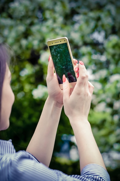 Girl takes on smartphone nature in a lush park in spring closeup