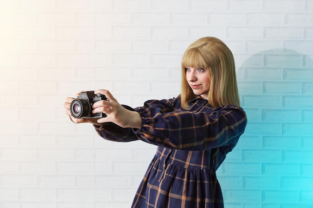 Girl teenager in dress holds retro camera in her hands makes snapshot and smiles