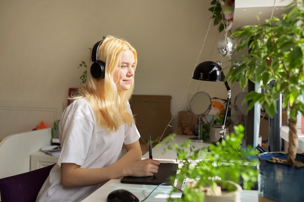 Girl teenager sitting at home drawing on computer using graphics tablet