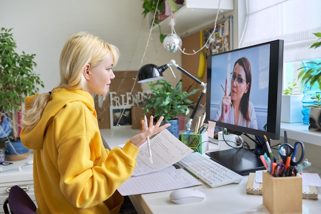 Girl teenager studies sitting at home using computer talking online with female teacher