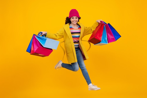 Girl teenager with shopping bags isolated on yellow backgound Winter shopping sale Run and jump