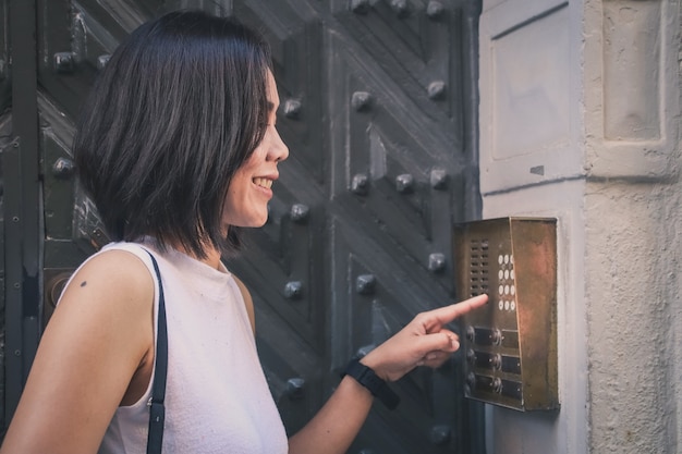 Girl that is pushing a button of the house intercom outdoors in front of a huge antique door.