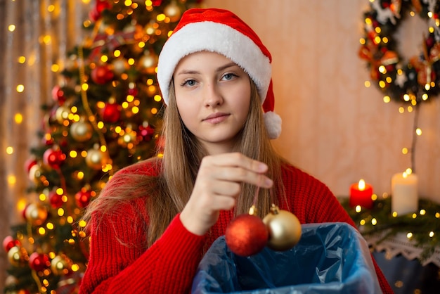 Girl throwing Christmas tree baubles away to recycle bin Using christmas decorations only one time then buy new