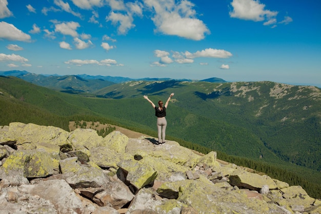 The girl at the top of the mountain raised her hands up Wide summer mountain view at sunrise and distant mountain range covered Beauty of nature concept