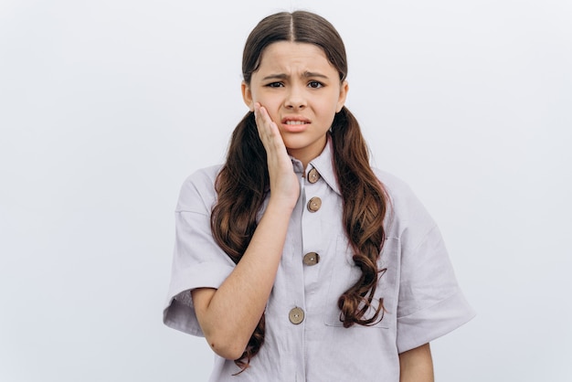 Girl touches her cheek with her hand, winces from a toothache. Cute little girl winced in pain on a white background