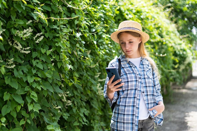 Girl tourist on a journey records a video on a mobile phone while standing near the greenery in the background A female traveler is streaming