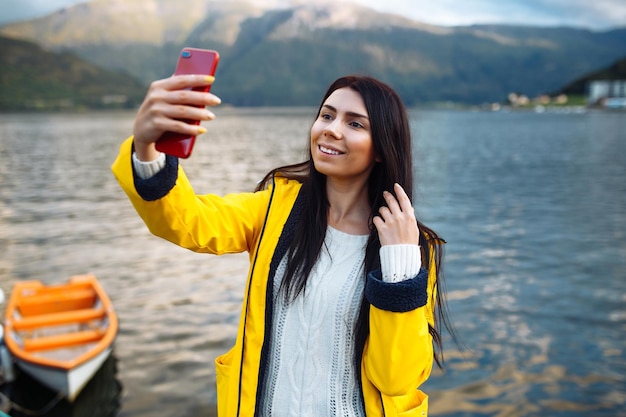 The girl tourist takes a photo on the phone by the lake in Norway Young woman takes selfie