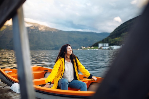 Girl tourist in yellow jacket is sitting and posing in a boat against the backdrop of the mountains