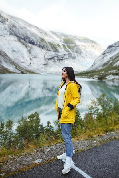 Girl tourist in yellow jacket posing on the lake in Norway Active woman relaxing in the Norway