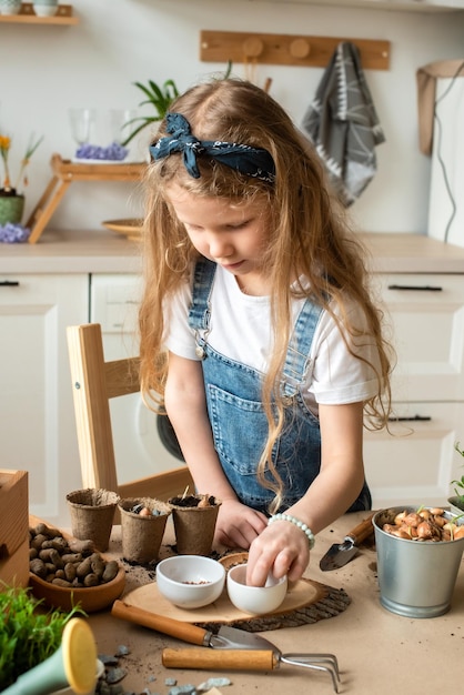 Girl transplants flowers and houseplants a child in a bandana plants bulbs hyacinths seeds