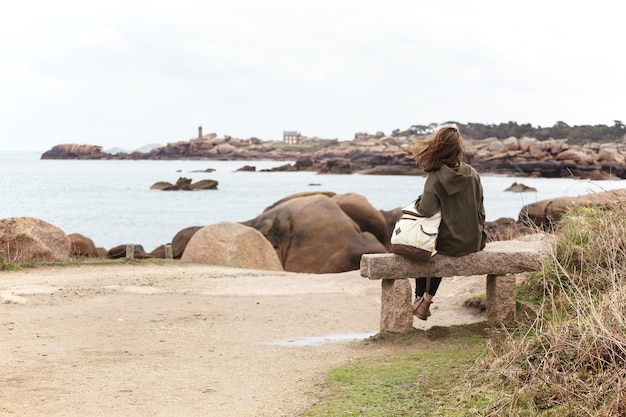 Girl traveler sits on a bench near the sea and the shore at  the Tregastel, Brittany. France