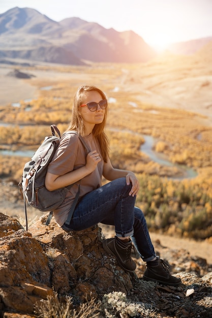 Girl traveler tourist sits on stone on  background of nature