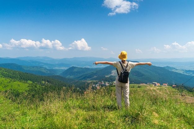 Girl traveler with a backpack stands with her arms outstretched in the mountains in summer