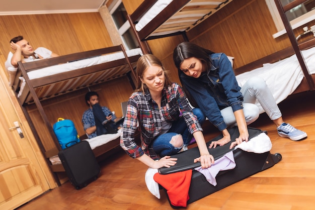 Girl trying helps girlfriend close valise.