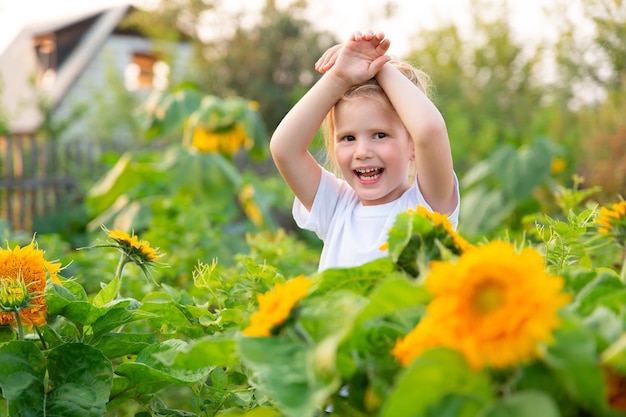 girl in Tshirt crossed her arms on her head stands in field of sunflowers and smiles