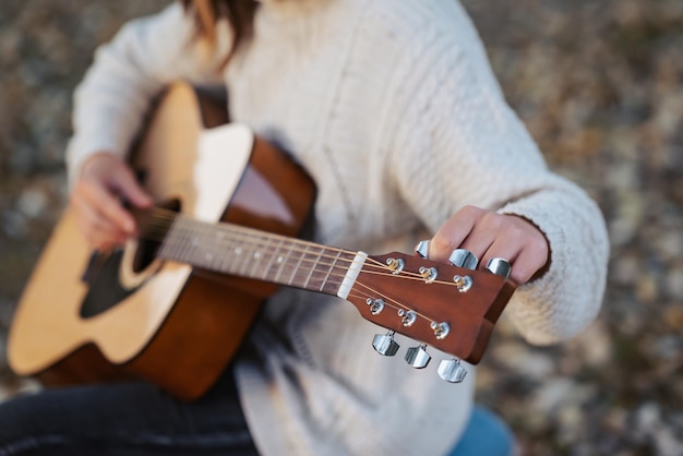 Girl tune acoustic guitar Close up of hands of a musician tuning guitar outdoor in autumn park