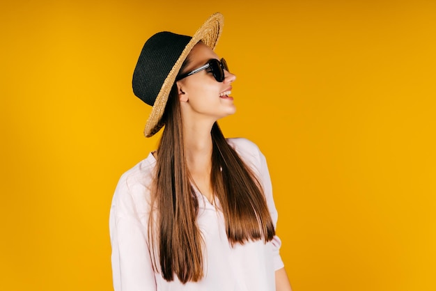 The girl turned her head to the side and smiles affably recognizing someone in the distance on her head a hat and black glasses on her eyes background yellow