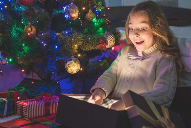 The girl unpack the gift on the christmas tree background. evening night time