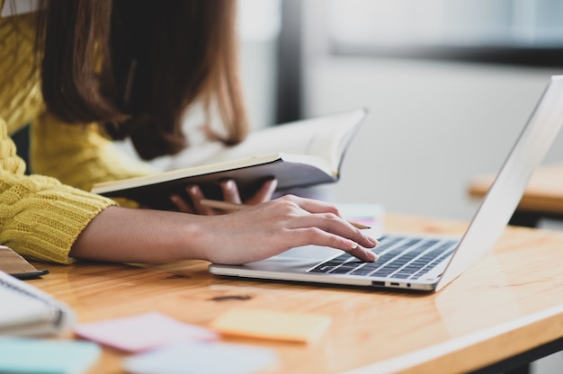 Girl using laptop and holding a book in hand ,She searched for information to learn, Online learning, Searching for information from the Internet.