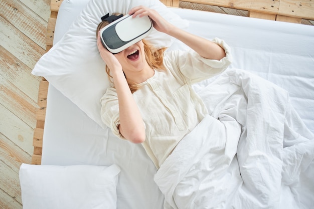 The girl in the virtual reality helmet on the bed