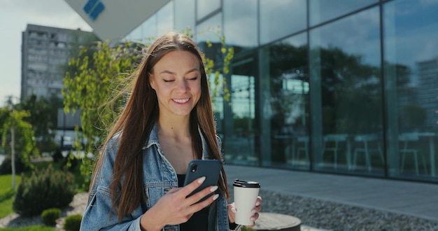 Girl walking with smartphone and coffee cup Beautiful woman using phone with takeaway coffee on street