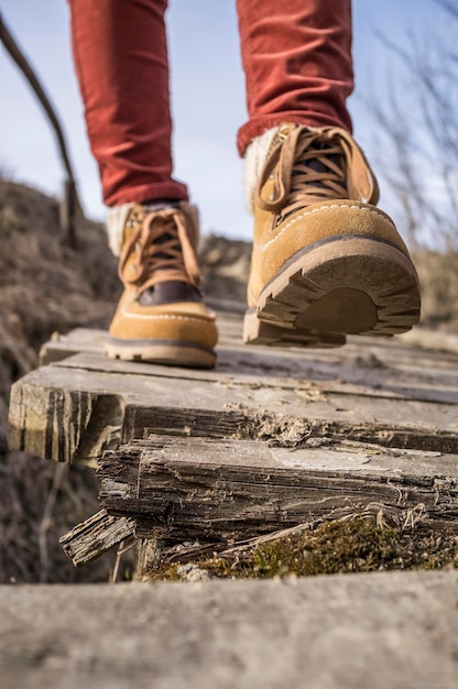 Girl walks along the old rotten wooden bridge in stylish boots on a sunny afternoon