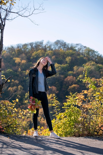 Girl walks in autumn park and enjoys a warm day. Portrait of happy girl student on beautiful autumn park. Vertical frame.